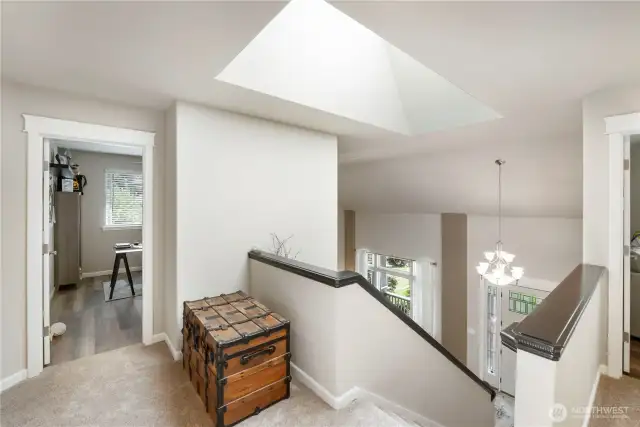 Upstairs Landing & Skylight: Bright and welcoming upper landing features a dramatic skylight, plush carpet, and a view down to the entryway, offering a perfect transition space between bedrooms and bonus rooms.