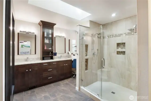 The primary bathroom was designed with comfort and style in mind—from the custom tile walk-in shower with built-in seat and dual niches to the dual vanities and abundant cabinet space. A well-placed skylight keeps the space naturally bright while enhancing the serene feel of this private retreat.