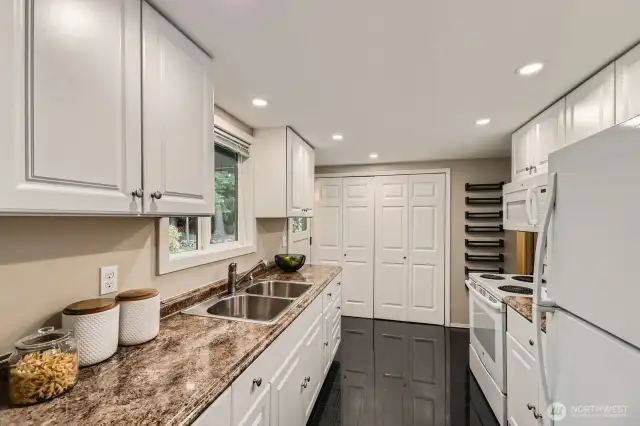 A beautiful kitchen with tile floors, white cabinetry, stainless steel sink and beautiful countertops, with a window looking into the tranquil back yard. The door leads to to the entertaining back deck.