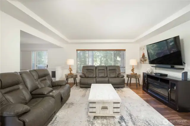 Spacious living room with large window (9’4”W x 4’7”H) and walnut shades. Features decorative rail trim and a tray ceiling for added character.