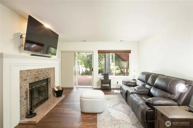 Cozy lower-level living room includes a wood fireplace with glass door enclosure (cleaned Fall 2024). Brick hearth and 5’ wide white wood mantle. Sliding glass door to backyard with built-in pet door (18”H x 10”W).