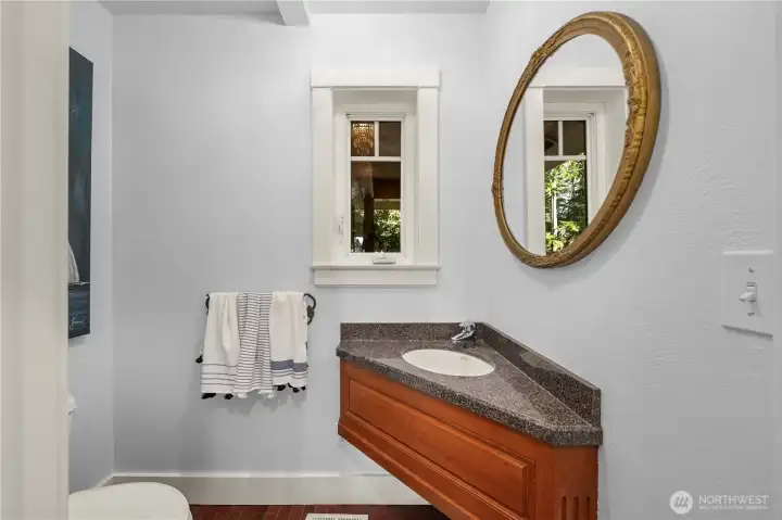 The main floor powder room features a carved custom cabinetry and a late antique mirror, brushed walls in a coastal blue.