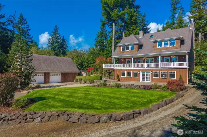 A great view showing the back of main house and the complementary style of the lower level separate guest quarters and detached garage and shop.