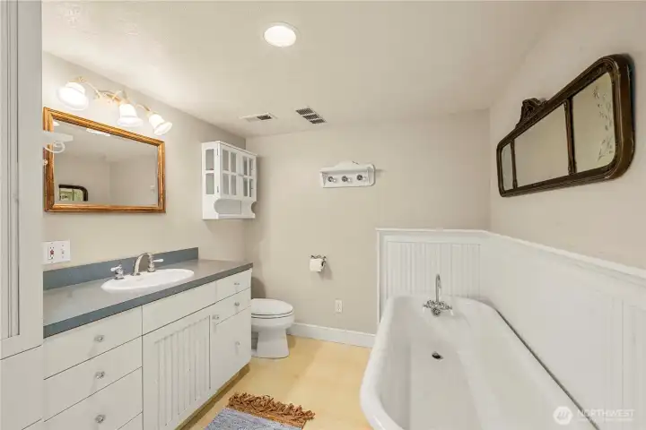 The lower level guest quarters bath features an antique claw foot tub and coastal bead bath vanity and heirloom accents.