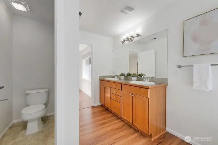 Primary ensuite features a double-sink vanity with modern finishes, a large framed mirror, and warm natural light that enhances the clean, contemporary design. Thoughtful details, including a separate toilet area and generous counter space, create a functional and comfortable layout. It’s a well-appointed extension of the primary suite, designed for everyday ease and a touch of luxury.