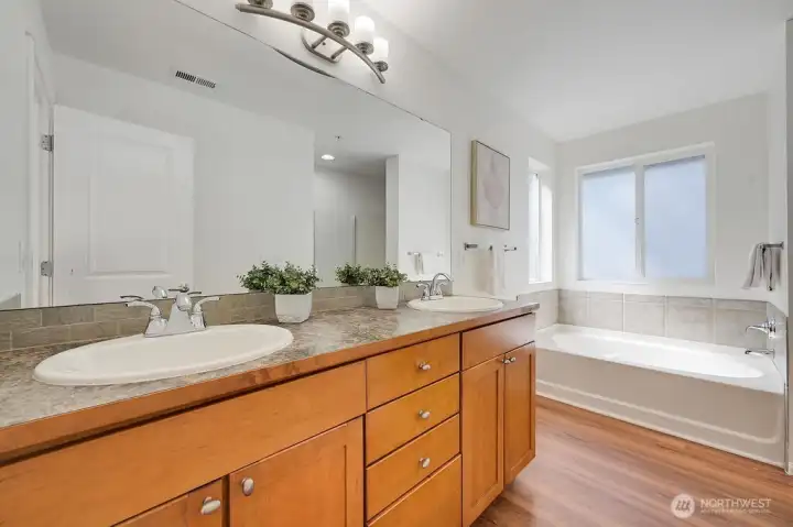 The primary suite is complemented by a bright and beautifully designed ensuite featuring a double-sink vanity, modern lighting, and warm wood-tone flooring. A soaking tub sits beneath a frosted window that brings in soft natural light while maintaining privacy, creating a spa-like feel. Clean lines, contemporary finishes, and a thoughtful layout make this an inviting extension of the primary retreat.