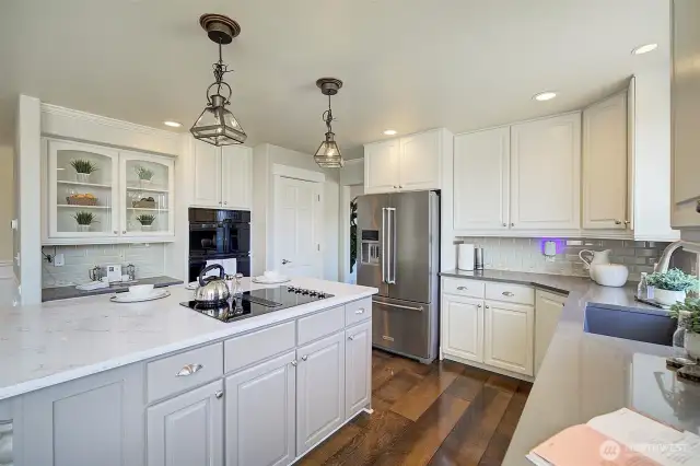 The stunning kitchen includes glass front cabinets for accent, quartz countertops, tiled backsplash, a large island, newer appliances and a convenient walk-in pantry closet.