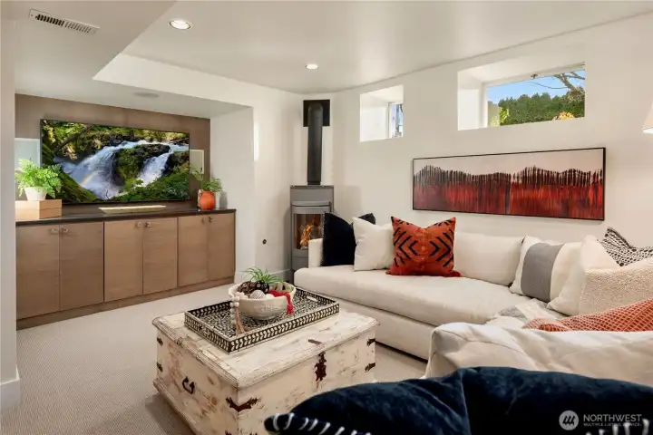 Cozy lower-level family room featuring a modern fireplace, built-in media storage and an inviting layout ideal for movie nights or relaxing evenings.