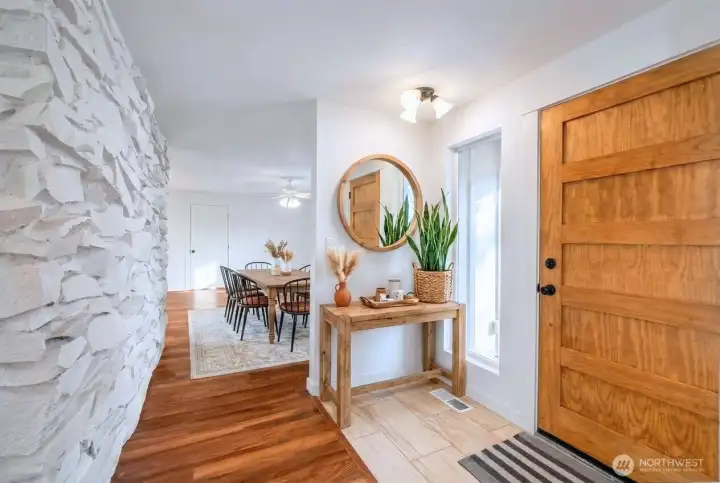 View of the front entryway with solid wood door. The back wall to the fireplace on the left provides architectural interest. Heading forward leads you into the dining room with propane fireplace and lots of windows and natural light. The kitchen lies to the left.