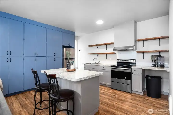 Close up view of open-concept kitchen with stainless steel appliances and abundance of storage space with open shelving and built ins. Nice sized island with seating.