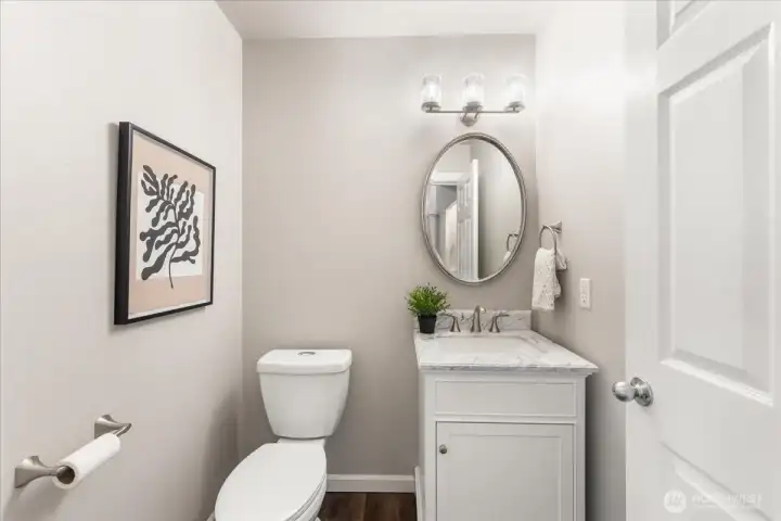 The updated half bath features new lighting, a marble vanity, and a new commode, adding a fresh and modern touch.
