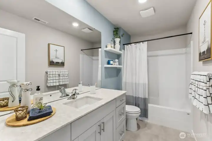 Hall bathroom with modern quartz countertops and soft close doors on shaker style cabinets. Actual home is under construction. Colors, materials, and features may vary. See site agent for details.