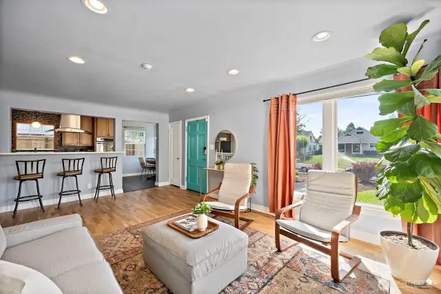 Living space with abundant natural light coming through picture windows. Looking out toward front door and kitchen space