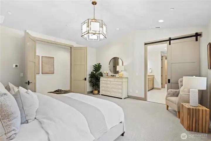 French door entry to sophisticated primary bedroom with vaulted ceiling. Barn-style door leads to luxurious ensuite bathroom.