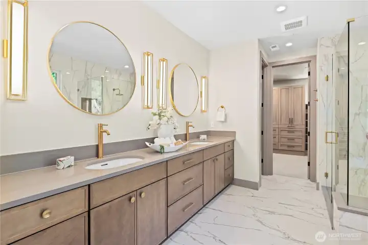 Elegant bathroom with dual vanities, extended-length slab quartz countertops, under counter sinks, beautiful gold-framed individual mirrors and complimentary sconce lighting.