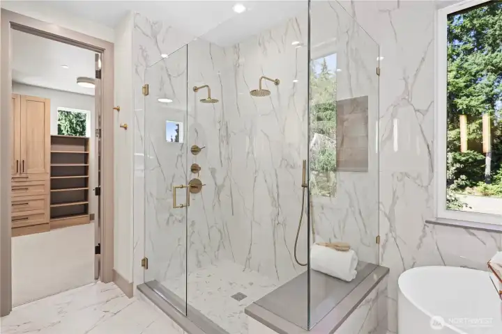 Large shower with floor-to-ceiling tile walls, shampoo niche, two shower heads, one with hand wand, bench lined in slab quartz, sleek frameless glass shower enclosure. Cozy heated floors. Private water closet is bidet-ready with nearby outlet. You'll notice Hamish Anderson Custom Homes line their shampoo niches with a slab sill as well as the window sill near the tub in this luxurious bathroom.