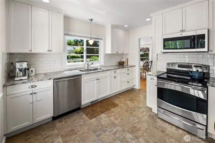 Updated kitchen features granite counters, white cabinetry, subway tile backsplash, stainless appliances, and abundant storage.