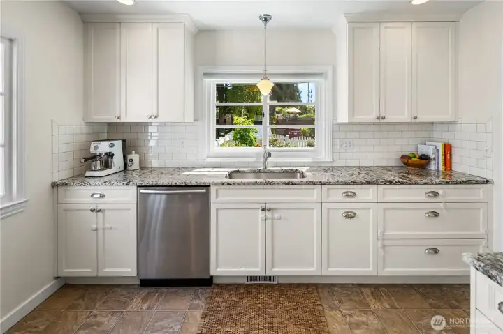 Updated kitchen features granite counters, white cabinetry, subway tile backsplash, stainless appliances, and abundant storage.