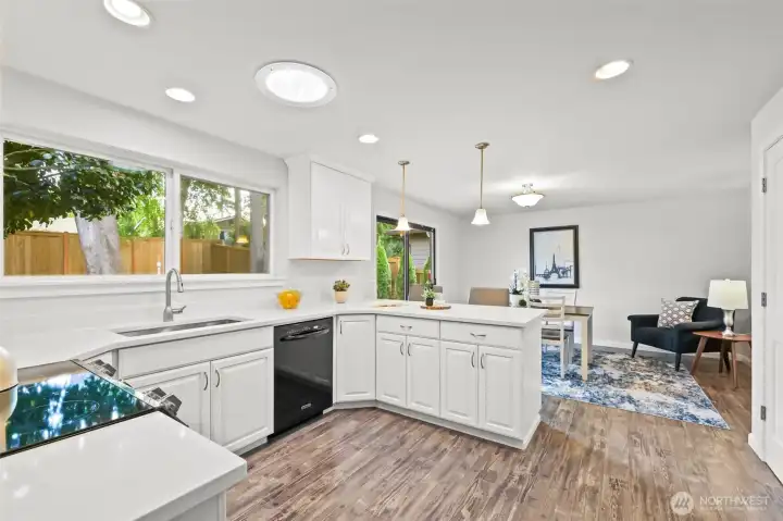 The kitchen has been thoughtfully updated with white cabinetry, expansive quartz counters, and modern lighting. Generous windows frame views of the backyard, creating a bright and cheerful environment for meal preparation.