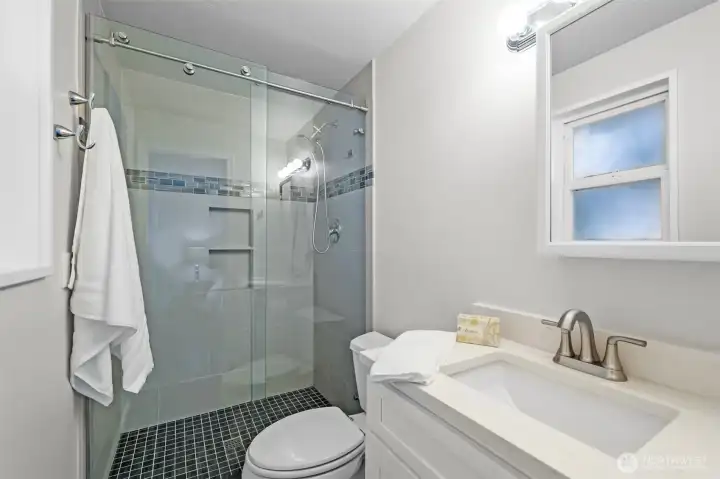 The primary bathroom includes a modern three-quarter layout with an updated vanity, stylish fixtures, and a walk-in shower with sliding glass doors.