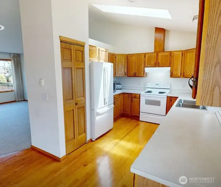 Natural light pours into the kitchen through the skylight, highlighting warm hardwood floors, ample storage, and an efficient layout.