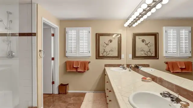 Large primary bathroom with gleaming floors and tile countertops. His and her sinks. Huge walk in custom dual head shower. Toilet has it's own door for privacy.