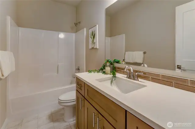 This beautifully appointed full bathroom includes a vanity with a below quartz surface mounted sink and easy-to-clean bath/shower