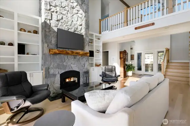 Floor to ceiling stone firplace with thoughtful built in This perspective highlights the home’s open layout, elegant staircase, and grand entry—all framed by breathtaking saltwater views that bring the beauty of Puget Sound indoors.