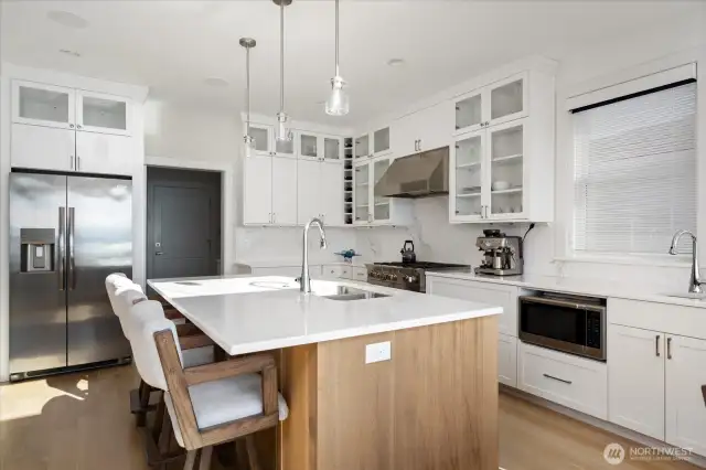 This beautifully designed wood island serves as the heart of the kitchen. Equipped with a sink, dishwasher, and seating, it blends functionality with style, providing a perfect workspace and casual dining area. Its warm wood tones contrast elegantly with the surrounding white cabinetry, creating a visually striking and practical centerpiece for cooking, entertaining, and enjoying waterfront views.