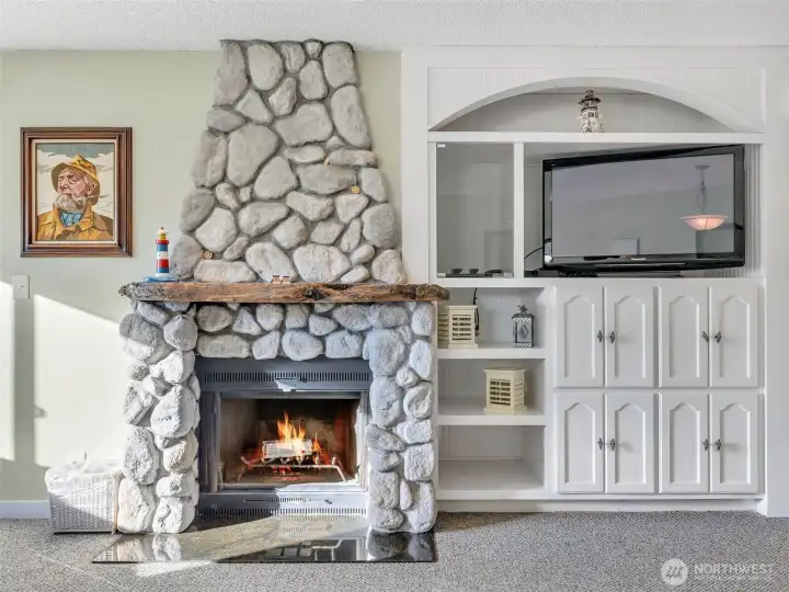 Custom river-rock fireplace with cedar driftwood mantel and built-in storage and entertainment cabinet.