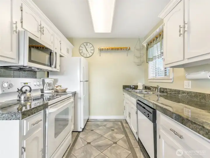 Kitchen of unit 420. Granite-tile countertops, oven/range, microwave, dishwasher, refrigerator, and sink with garbage disposal.