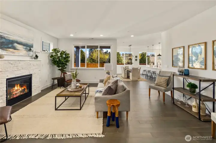 Great Room  The great room showcases open concept living with clean architectural lines and expansive rear windows that draw in natural light and frame the private backyard setting. A modern fireplace with textured surround anchors the space, creating warmth and visual contrast against wide plank flooring. The layout flows seamlessly into the kitchen and dining areas, supporting effortless gathering and everyday functionality. Designed for contemporary living in Bothell’s Canyon Park area, this space reflects the elevated finishes and thoughtful flow expected in luxury new construction within the Northshore School District.    These photos are from a past Robinson Plan at a different community, so overall plan, colors, building orientation, finishes, home outlook, and other details can and WILL vary. All photos, renderings, site maps, and floorplans are for visualization purposes only.