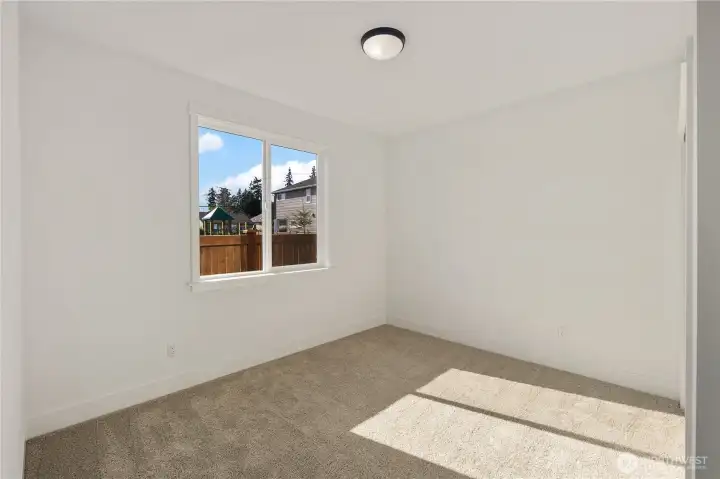 Main Level Den / Guest Bedroom  This main level den offers flexible living space with clean lines and abundant natural light. A large window frames the backyard outlook while soft carpeting and neutral tones create a comfortable setting for a home office, guest suite, or additional bedroom. The thoughtful placement on the main level enhances everyday convenience and accessibility.    Situated in Bothell, Washington near Canyon Park, this versatile room supports modern living within a Pacific Northwest contemporary home. The adaptable layout reflects the intentional design approach found in luxury new construction served by the Northshore School District.    These photos are from a past Robinson Plan at a different community, so overall plan, colors, building orientation, finishes, home outlook, and other details can and WILL vary. All photos, renderings, site maps, and floorplans are for visualization purposes only.