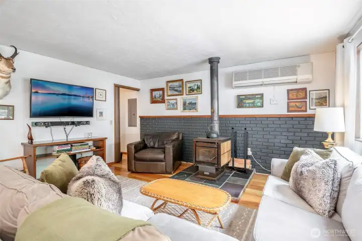 Inviting front entry opens into a cozy living room with wide plank wood floors and a wood burning stove. A mix of vintage charm and lodge-style warmth is enhanced by the brick accent wall.