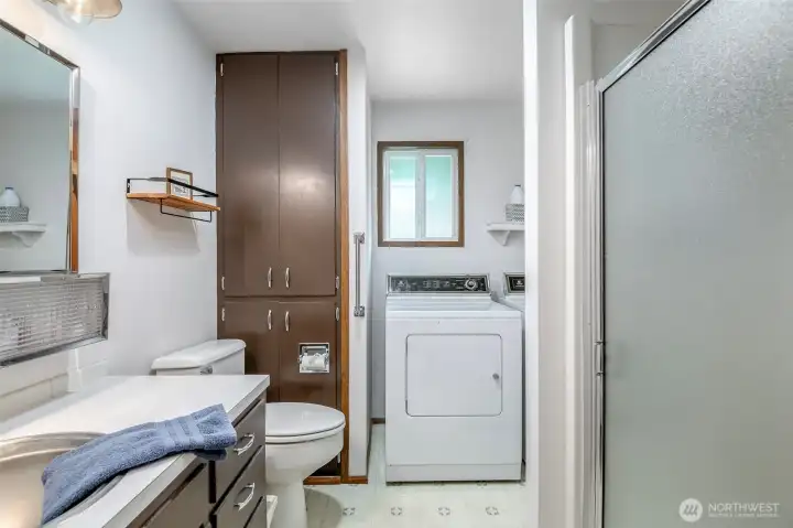 Main floor bathroom and laundry combo with full-size washer/dryer, built-in linen storage, and a walk-in shower—efficient and practical layout.