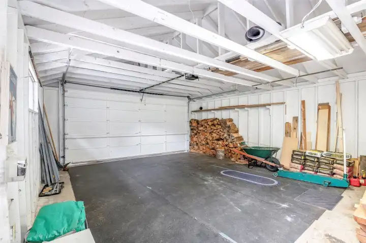 Oversized detached garage with room for two cars, plus an additional bay which would make a great workshop, storage space, or place to park your golf cart. Includes stacked firewood and shelving, ideal for outdoor gear or project materials.
