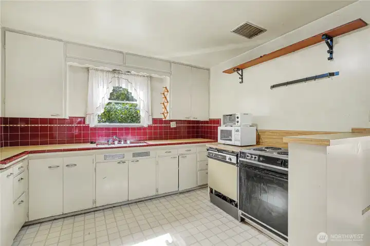 Retro kitchen with original cabinetry, and red tile backsplash, offering a functional layout with excellent potential for renovation or customization.