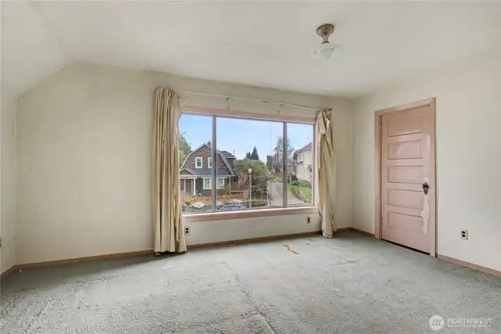 Bright upper-level room with original finishes and a large window offering natural light and neighborhood views—an inviting space ready for renovation or personalization.