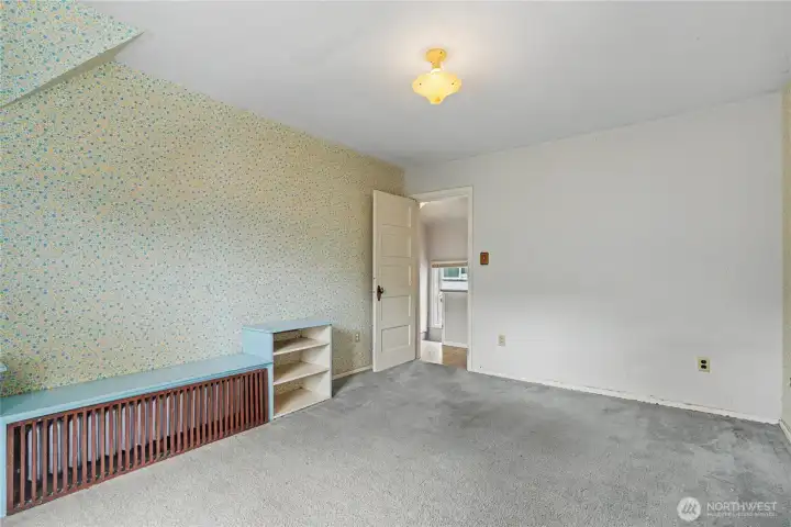 Cozy room featuring vintage wallpaper, sloped ceilings, and built-in radiator cover, offering classic character and a solid foundation for future updates or creative redesign.