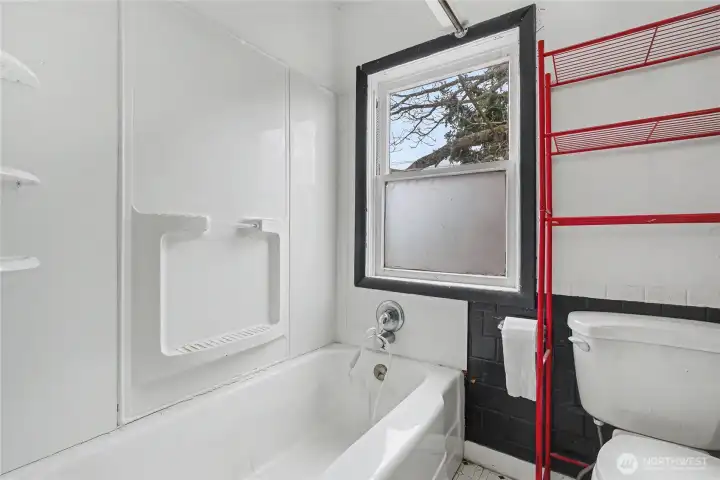 Full bathroom featuring a tub/shower combo with built-in shelving, classic tile accents, and a window for added light and ventilation—an efficient space with opportunity for modern upgrades.