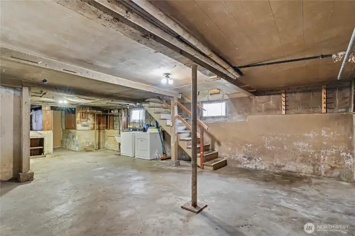 Unfinished basement with exposed beams, concrete floors, and laundry hookups—ideal for storage, workshop use, or future finishing to expand usable living space.