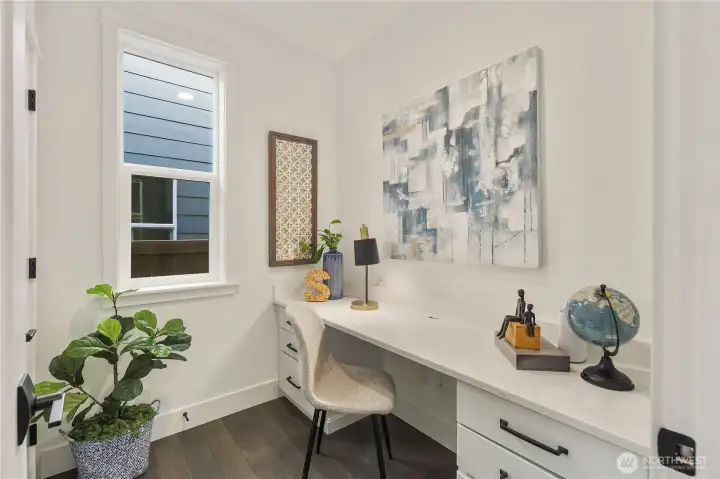 Main Level Pocket Office  This main level pocket office delivers a dedicated workspace without sacrificing the home’s open flow. A built-in desk with quartz surface and integrated cabinetry provides clean, functional storage, while a large window brings in natural light to create a bright, focused setting. The efficient footprint supports productivity while maintaining architectural simplicity.    Located in Bothell’s Canyon Park neighborhood, this signature design element reflects the thoughtful planning associated with contemporary new construction. The flexible workspace enhances everyday livability within a modern home served by the Northshore School District.    These photos are from a past Robinson Plan at a different community, so overall plan, colors, building orientation, finishes, home outlook, and other details can and WILL vary. All photos, renderings, site maps, and floorplans are for visualization purposes only.