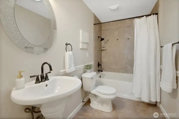 Guest bathroom offers a full tub and shower combo with ceramic tile surround, pedestal sink, easy to clean tilel flooring and chair moulding.