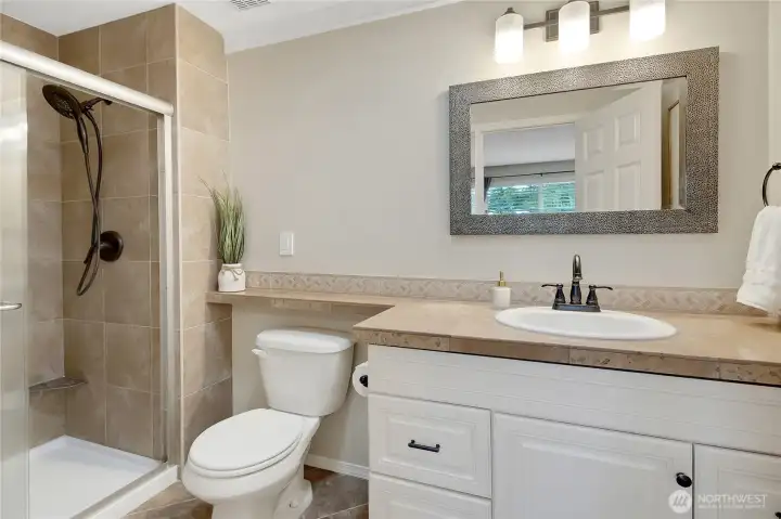 Primary bathroom has plenty of countertop space, storage, a glass shower door with a tiled shower surround, and a solar tube brings lots of natural light!