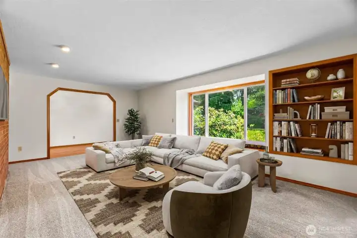 The living room with built in shelving. The view out the windows toward the line of Rhododendrons is amazing. (Virtually Staged)