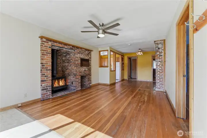 Living room area inside front entrance features original wood flooring, a brick wood stove hearth, ceiling fan, & access to the rest of the home.
