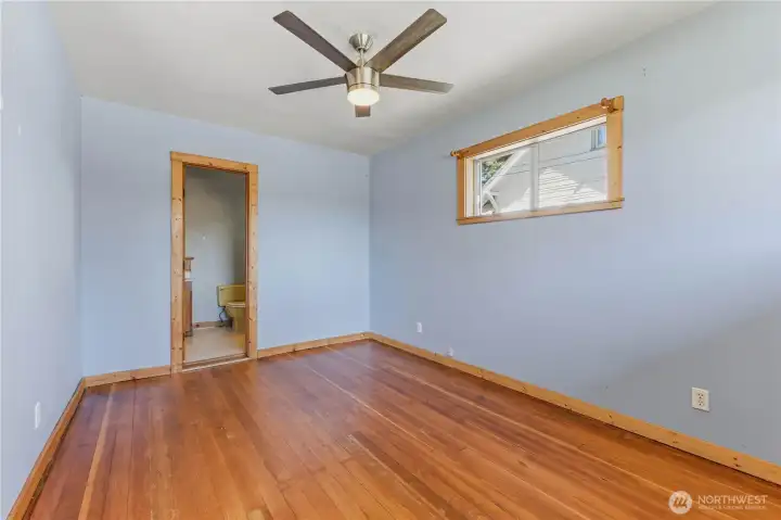 Primary bedroom suite is large with original hardwood floors, wood trim, ceiling fan, & ensuite full bath.