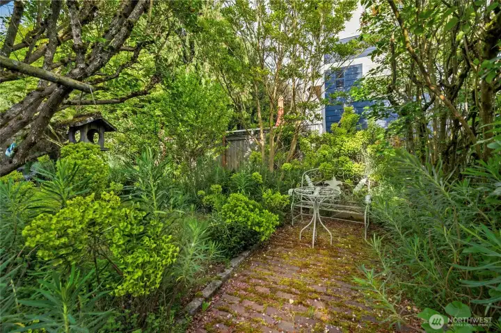 Mature landscaping designed for multiple outdoor garden 'rooms'.  Pictured here, tucked in the back corner of the property a brick patio for a furniture set.  Sit, listen and watch the little birds.  Truly unique and special property.