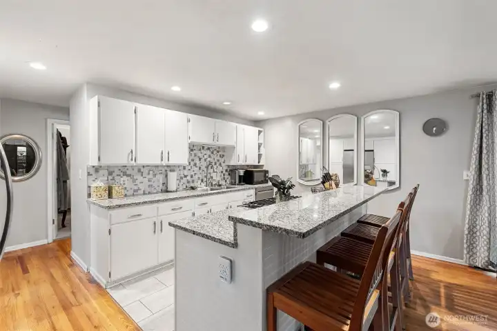 Updated kitchen with granite counters, white cabinetry, tile backsplash, recessed lighting, and oversized breakfast bar with seating.