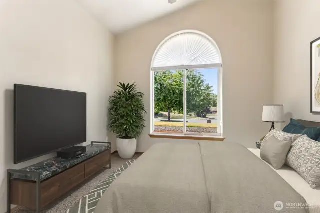 Virtually staged bedroom (staged here as an office) with carpet flooring and a half-moon, formerly called a lunette, window. Closet with built-in custom shelving and storage is to the left of the photo, vaulted ceilings and ceiling fan.